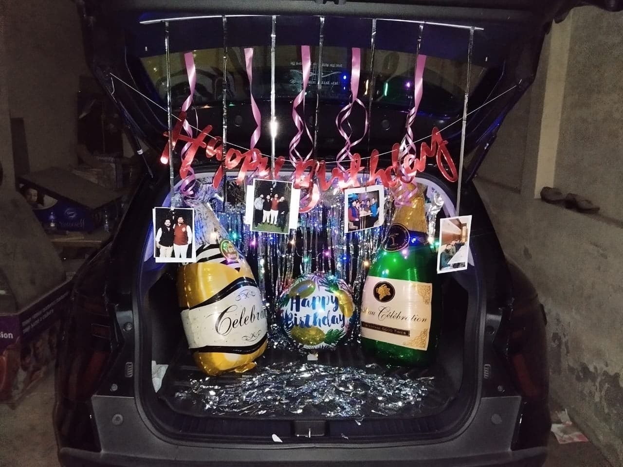 Car boot birthday surprise with a neon sign, foil champagne balloons and hanging photographs