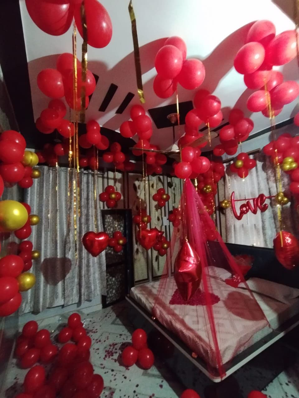 Bedroom anniversary surprise filled with red and gold balloons and a love neon sign
