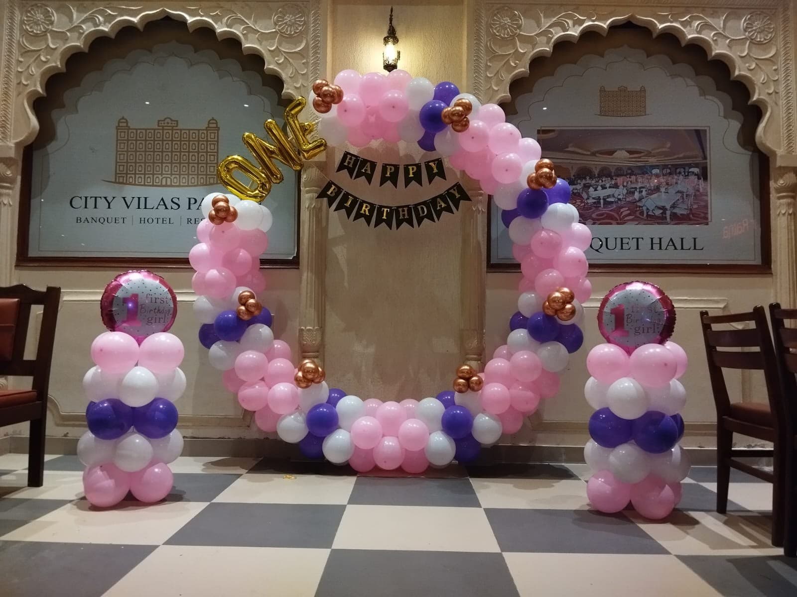 Pink, purple and white balloon ring arch with a Happy Birthday banner in a banquet hall