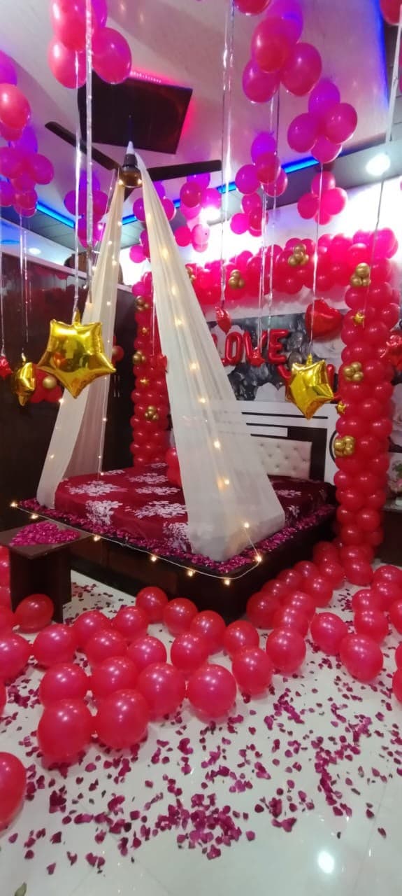 Romantic room setup with a white drape canopy, pink balloon pillars and rose petals