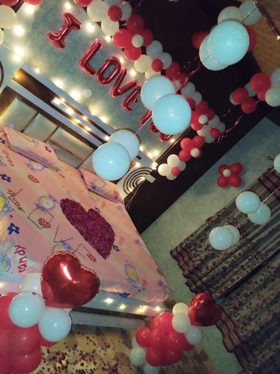 Room decorated with red and white balloons, fairy lights and an I Love You foil banner