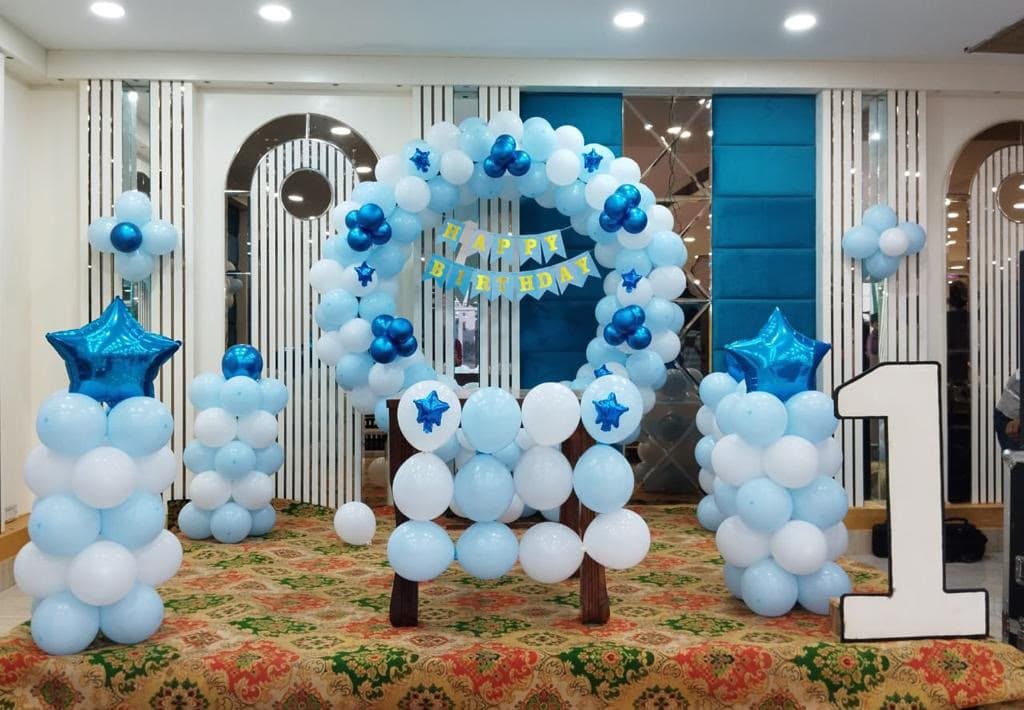 First birthday balloon arch in blue and white with a Happy Birthday banner and a giant number one