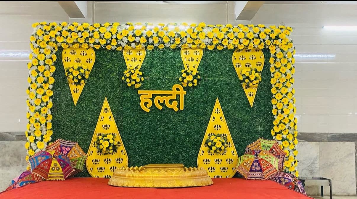 Green grass wall with a yellow floral border and golden Haldi signage