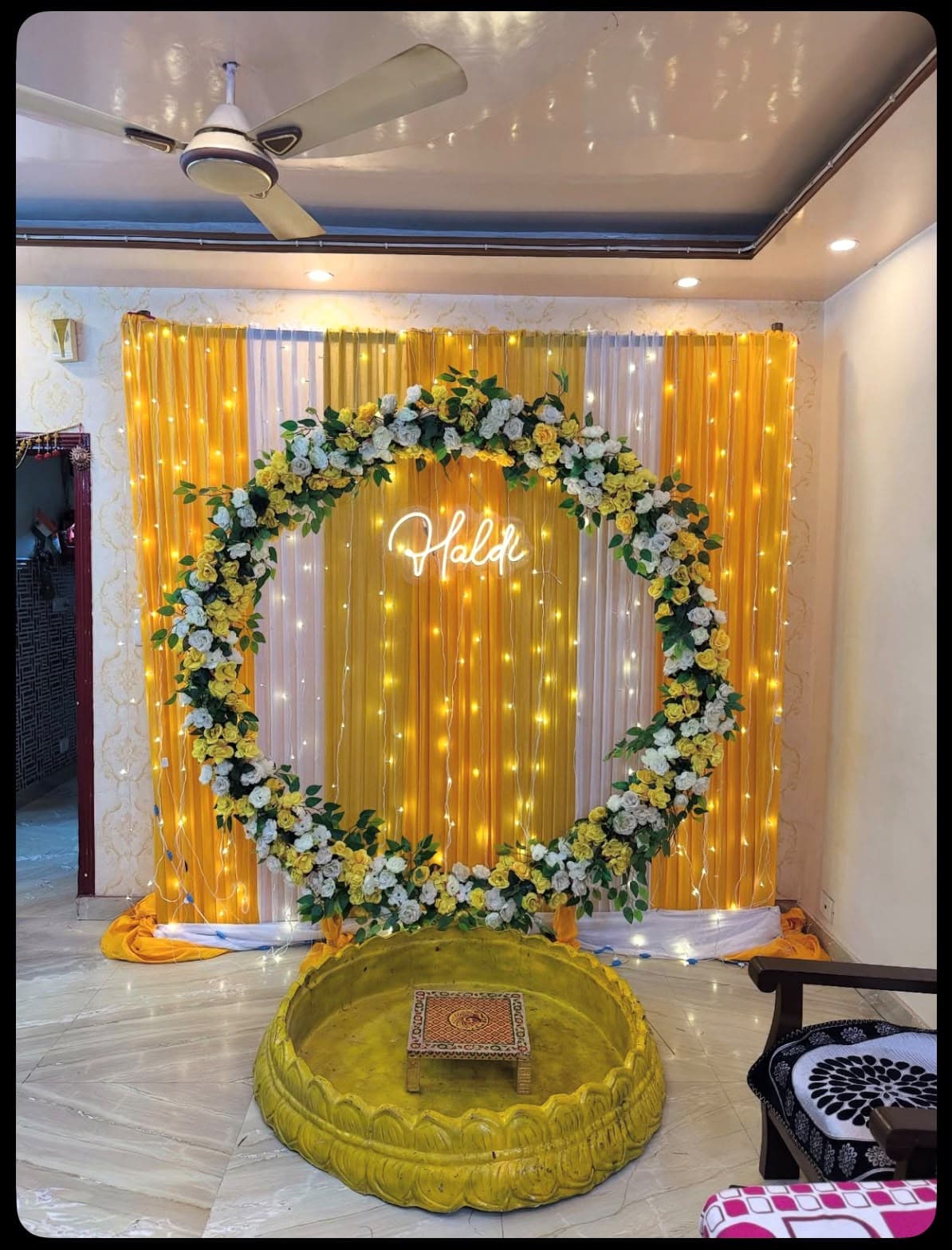 Haldi ring arch of yellow and white roses against a gold drape with a neon Haldi sign