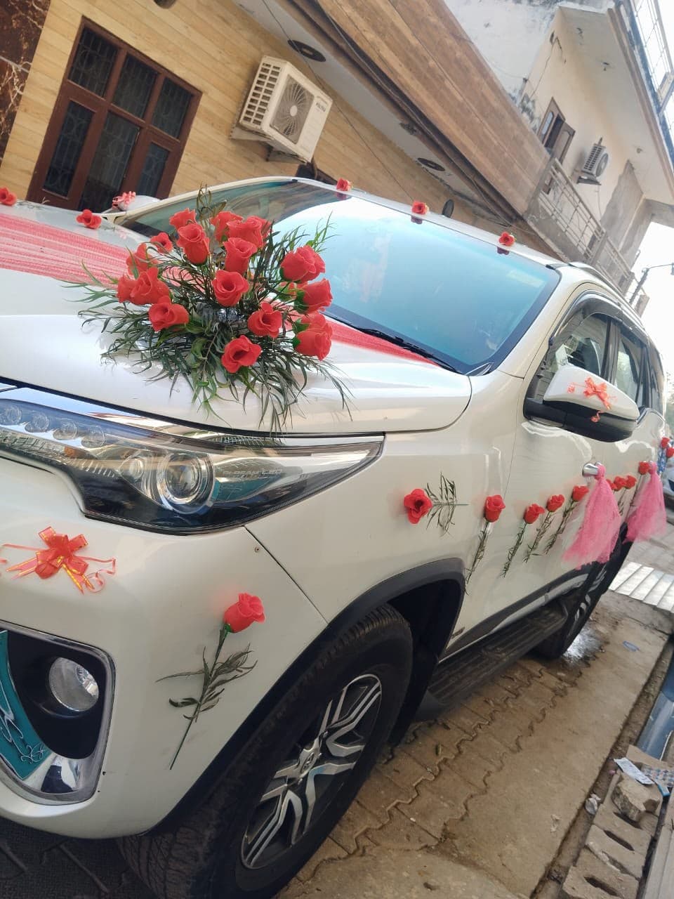 White wedding car dressed with a red rose bonnet arrangement and pink ribbon tassels